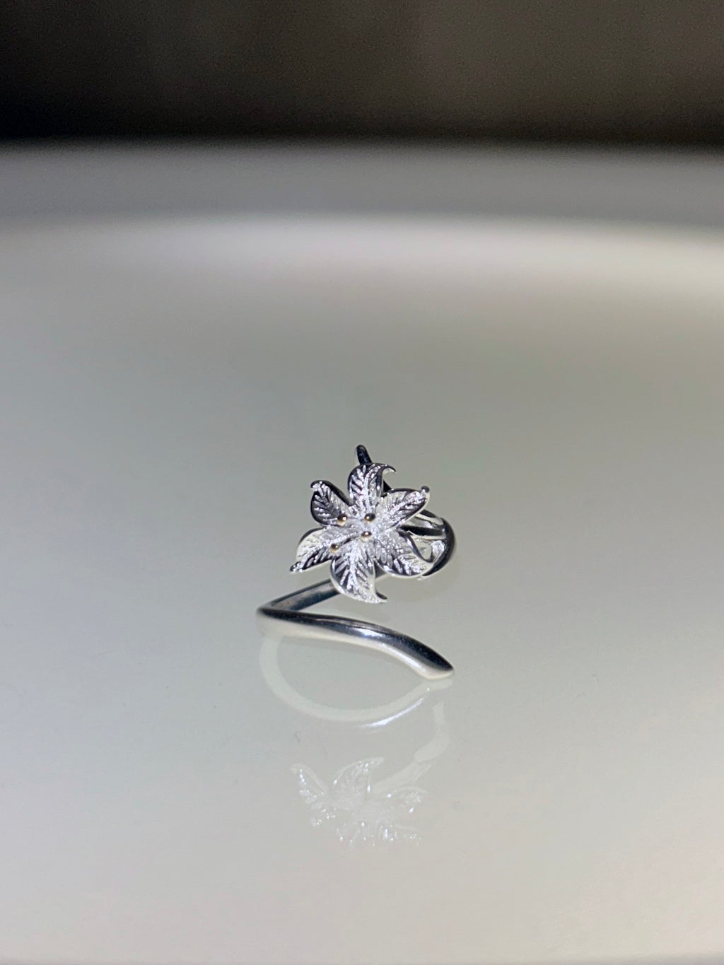 Silver ring with a floral design on a reflective surface