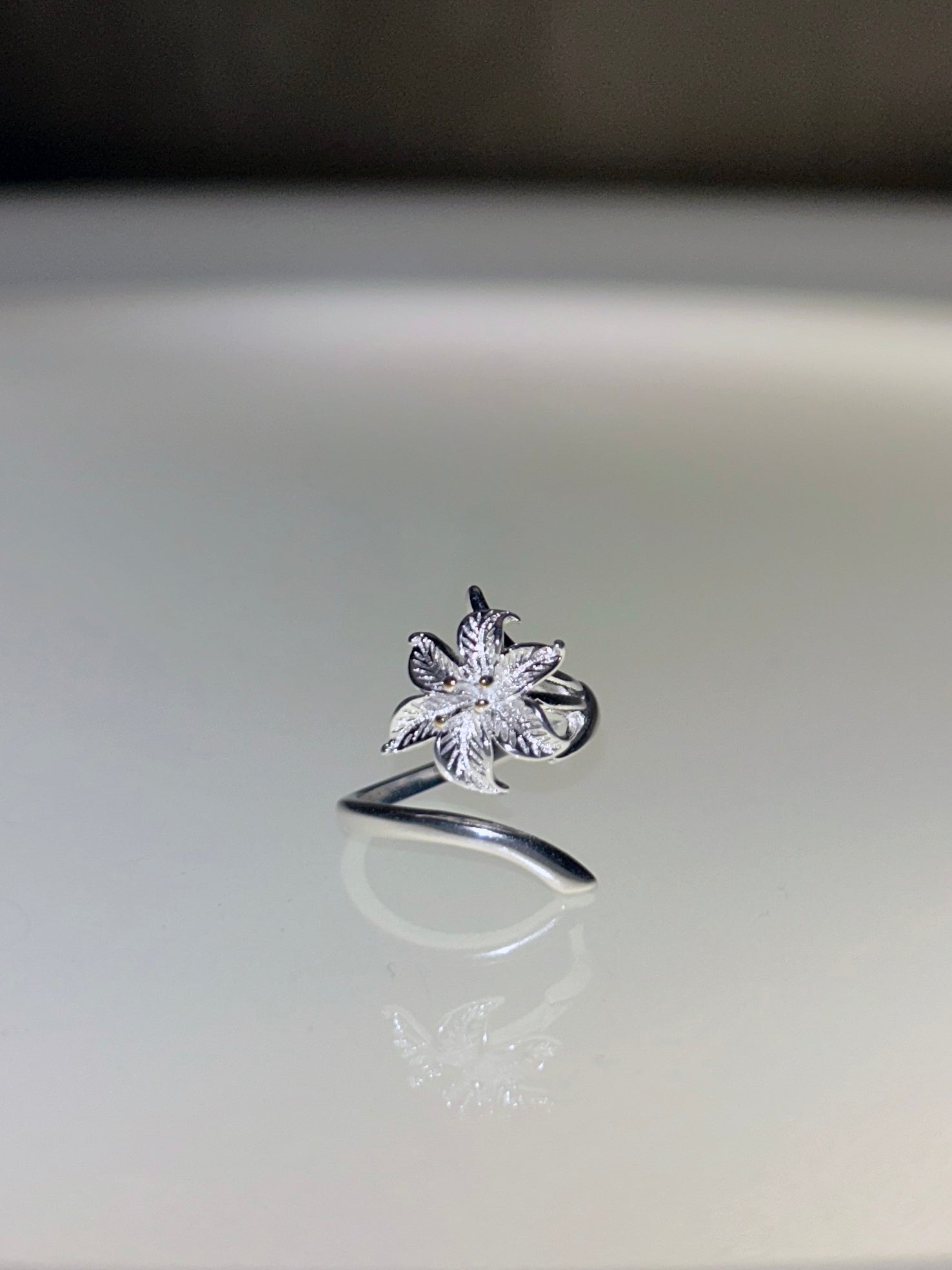 Silver ring with a floral design on a reflective surface