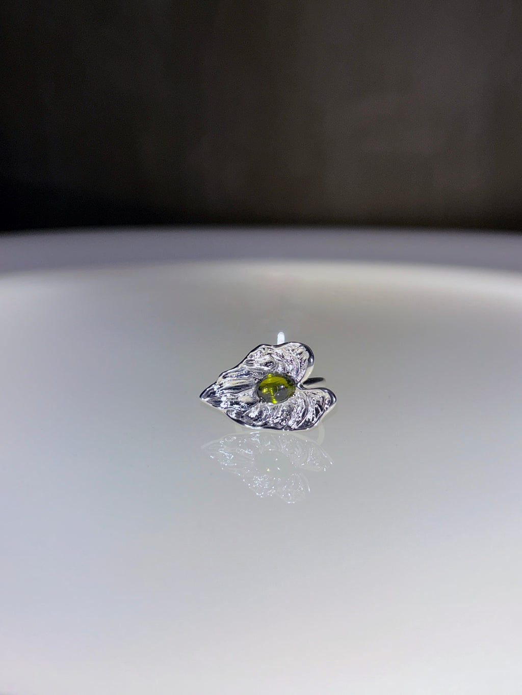 Silver ring with a green gemstone on a reflective surface