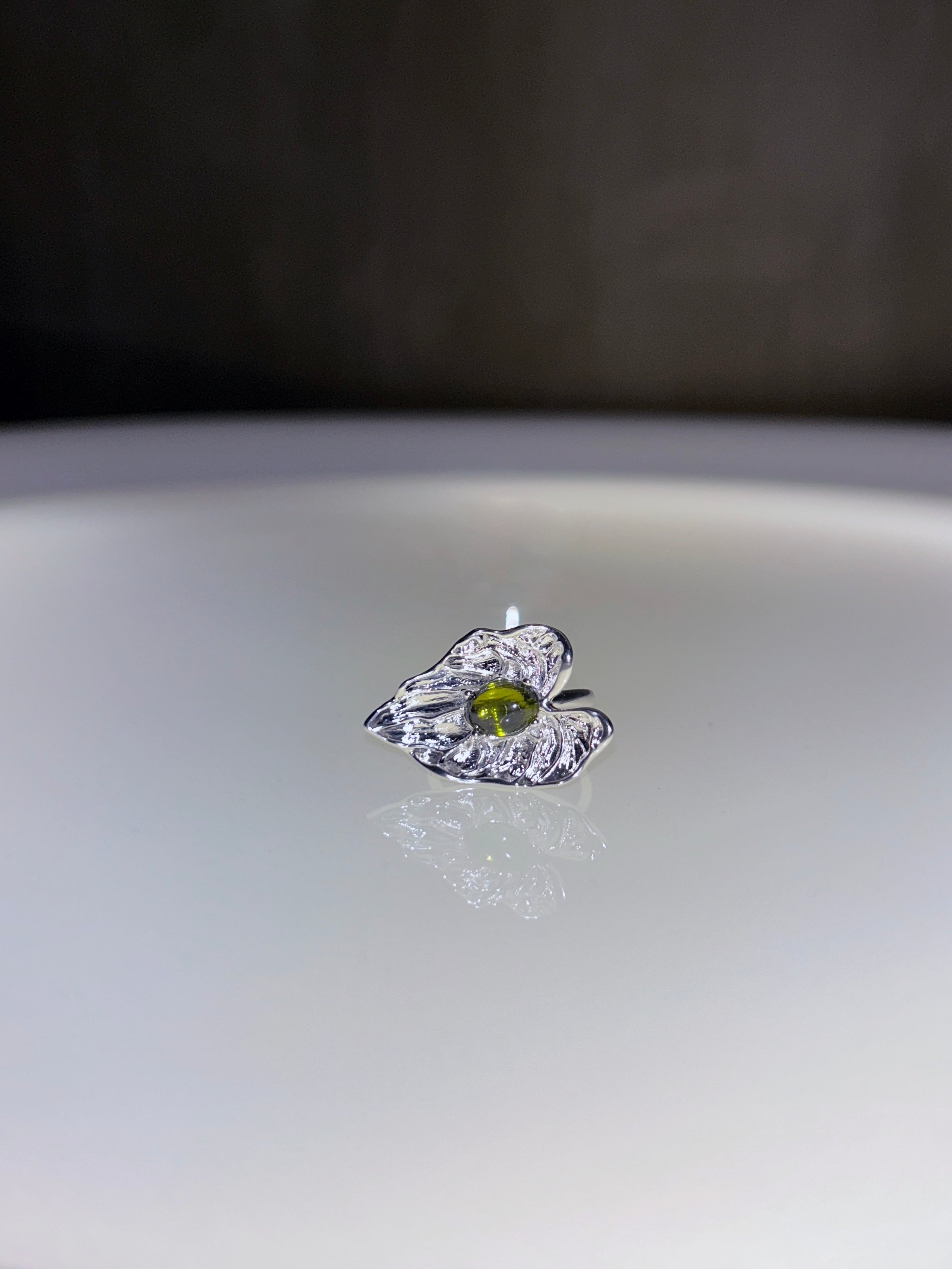 Silver ring with a green gemstone on a reflective surface