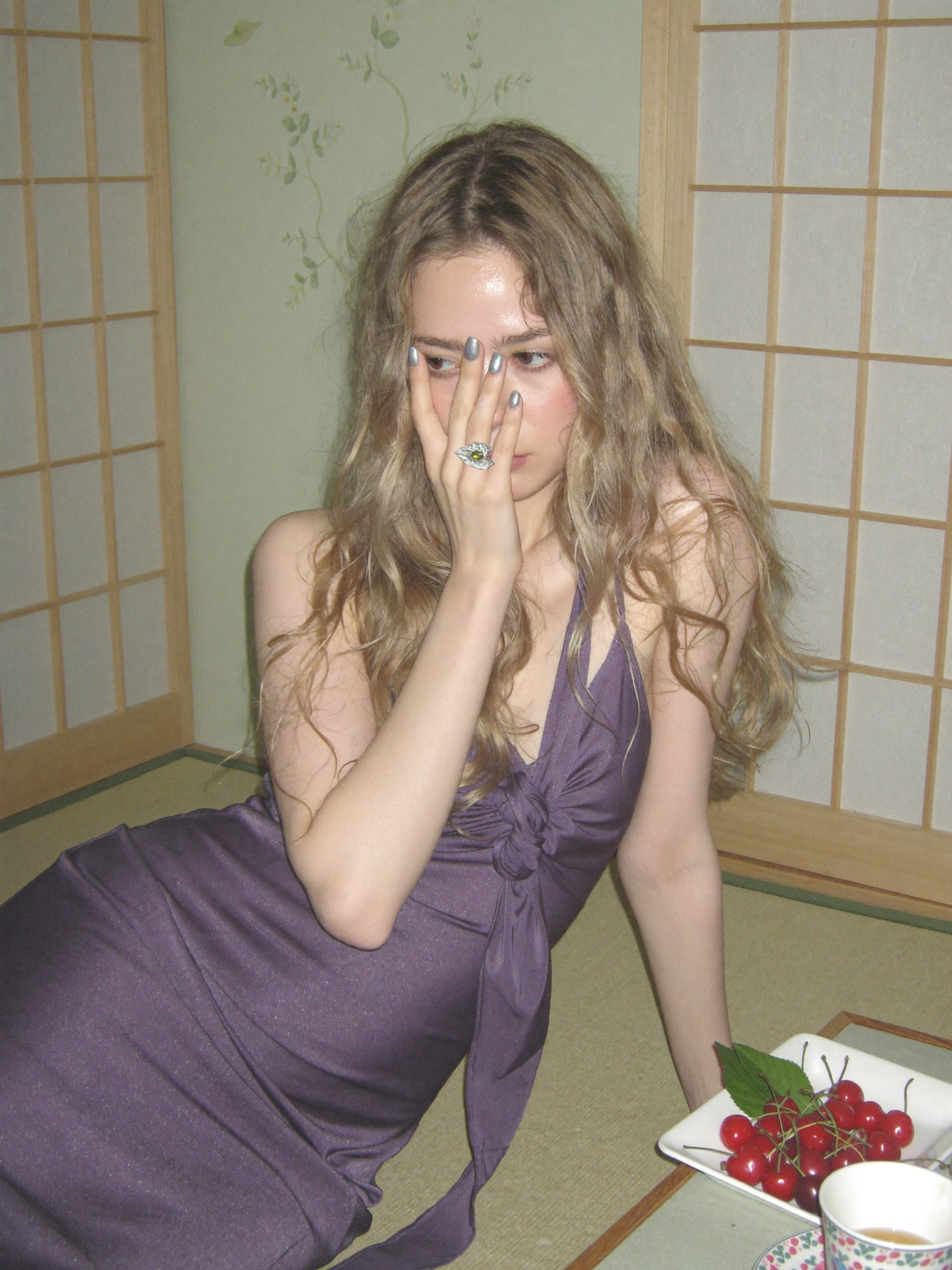 Woman in a purple dress sitting at a table with a plate of cherries in a room with shoji screens.